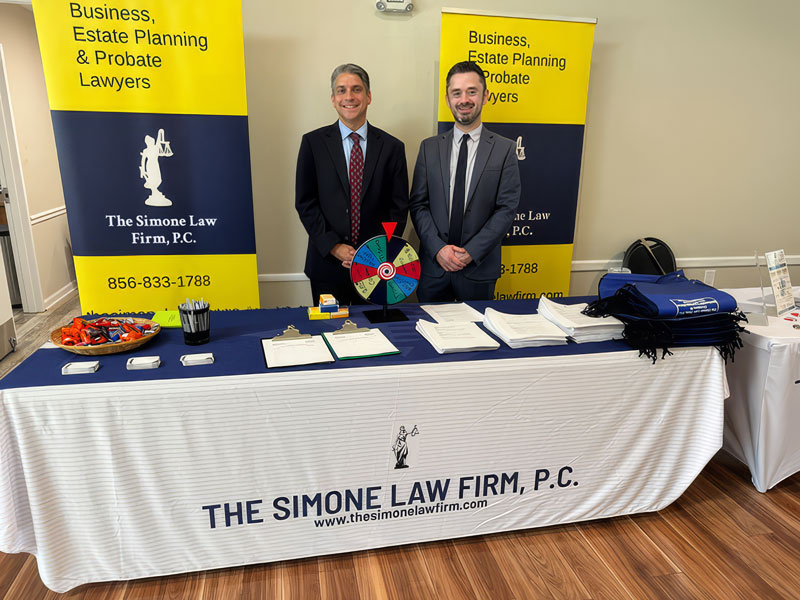 Group photo of The Simone Law Firm team at an event standing in front of a booth advertising the firm